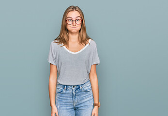 Obraz premium Beautiful young blonde woman wearing casual clothes and glasses puffing cheeks with funny face. mouth inflated with air, crazy expression.