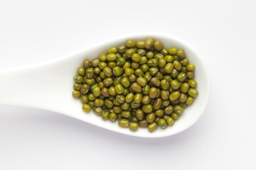 macro Close-up of Organic green Gram (Vigna radiata) or whole green moong dal on a white ceramic soup spoon. Top view