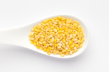 Macro Close up of Organic yellow Gram (Vigna radiata) or split yellow moong dal inside a ceramic white soup spoon. Top view 