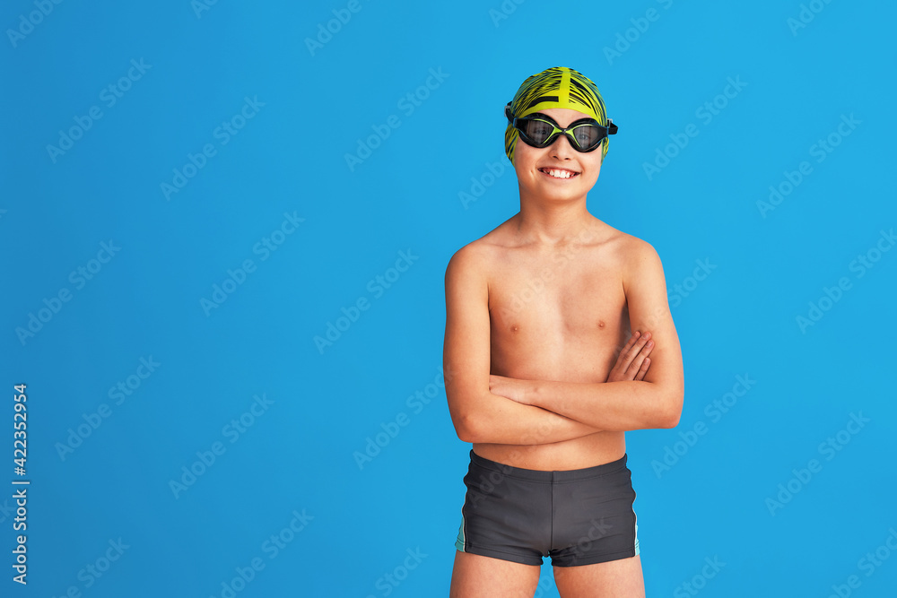 Wall mural portrait of a sporty boy child in a swimming cap, glasses and a bathing suit, on blue background. th