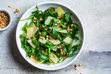 Arugula and parmesan salad with pine nuts in white bowl, top view. Italian cuisine concept.