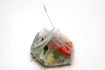 DEFOCUS. Earth day. Red and green plants flowers in a plastic bag on a white background. A dry blade of grass sticks out. Ecological problems. Out of focus