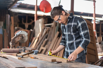 Carpenter man using ruler measuring tape wood plank at the carpentry workshop
