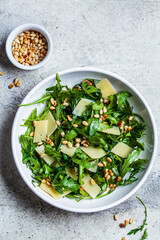 Arugula and parmesan salad with pine nuts in white bowl, top view. Italian cuisine concept.