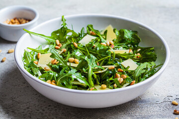 Arugula and parmesan salad with pine nuts in white bowl. Italian cuisine concept.