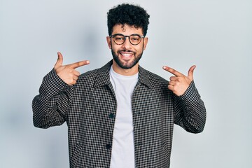 Young arab man with beard wearing glasses smiling cheerful showing and pointing with fingers teeth and mouth. dental health concept.