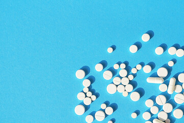 White tablets, pills and capsules on a sky-blue background with space for text. Medical background.