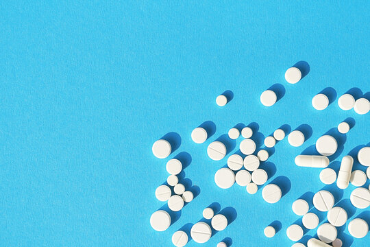 White tablets, pills and capsules on a sky-blue background with space for text. Medical background.
