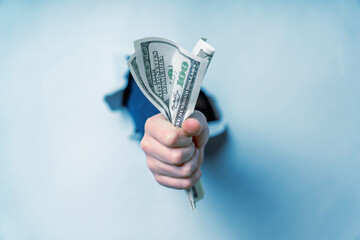 The best gift instead of flowers is money. Close up hand  giving US Dollar banknotes through torn paper wall.