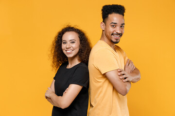 Young couple friends together team family african smiling happy man woman 20s in black t-shirt stand back to back with hands crossed folded look camera isolated on yellow background studio portrait