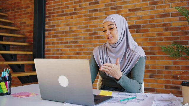 Young Muslim girl in a hijab has a video call with a laptop. Woman designer talks about her project, online design training