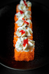  Japanese rolls with caviar and philadelphia cheese on a black plate close-up, selective focus, vertical photo