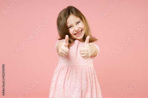 Little cute kid girl 5-6 years old wears rosy dress showing thumb up like gesture isolated on pastel pink background child studio portrait. Mother's Day love family people childhood lifestyle concept.