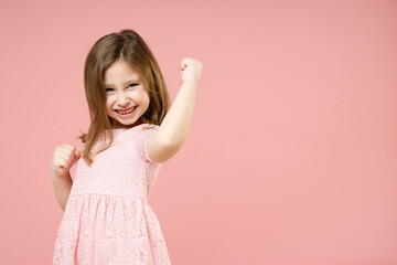 Little kid girl 5-6 years old wears rosy dress have fun doing winner gesture celebrate clenching...