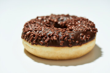 Unhealthy dessert. Close up shot of a freshly baked delicious chocolate donut with sprinkles on white background