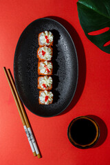  Japanese rolls with flying fish roe and philadelphia cheese on black plate and red background, vertical photo in modern style with hard shadows