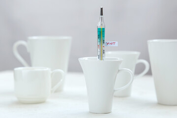 Many white cups on the table, one of them with thermometer with inscription Cosy