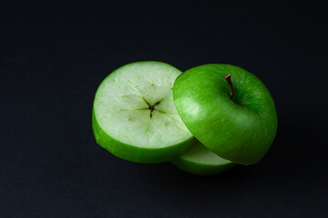 Green apple on a dark background. A cut green apple on a black background. Healthy food