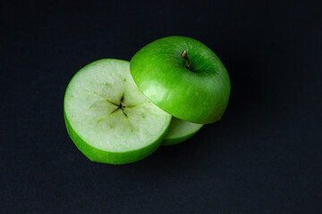 Green apple on a dark background. A cut green apple on a black background. Healthy food