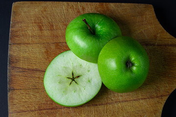 Green apple on a dark background. A cut green apple on a cutting board on a black background. Healthy food