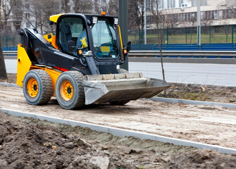 Little nimble road grader in motion on a sidewalk under construction in a light blur against the...