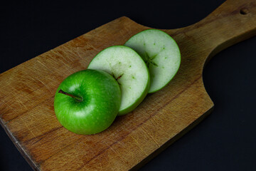 Green apple on a dark background. A cut green apple on a cutting board on a black background. Healthy food