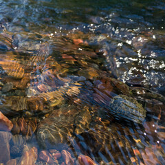 Clean and clear wavy water in stream, stones at the bottom of shallow creek, refraction of light