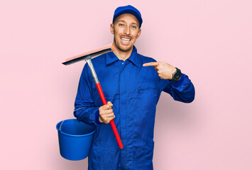 Bald man with beard wearing glass cleaner uniform and squeegee pointing finger to one self smiling...