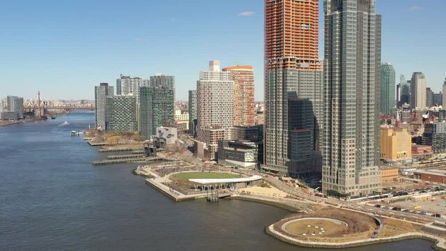 A high angle view looking north over the East River on a sunny day. The drone camera dolly out and pan left, looking up the river to the Upper East side of Manhattan, NY
