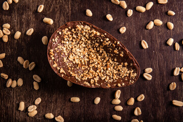 Stuffed chocolate easter egg with peanut and caramel on a wooden table with lots of peanuts around. Top view.