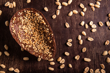 Stuffed chocolate easter egg with peanut and caramel on a wooden table with lots of peanuts around. Top view.