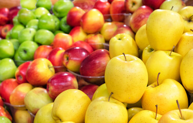 Yellow apples are sold in the market against the background of various other varieties.
