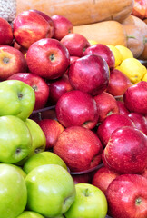 Red and green apples are stacked in a heap on the market counter and attract the attention of buyers.
