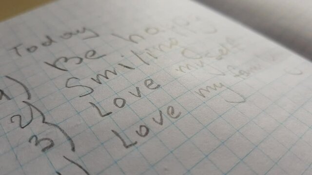 Text in checkered notebook. Today - be happy, smiling, love myself, love my family