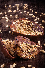 Stuffed chocolate easter egg with peanut and caramel on a wooden table with lots of peanuts around. Cracked.