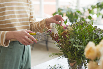 Close up of unrecognizable woman cutting plants while arranging floral compositions in workshop, copy space