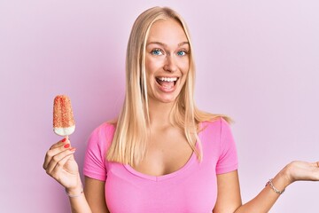 Young blonde girl holding ice cream celebrating achievement with happy smile and winner expression with raised hand