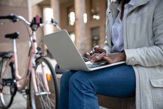 Young woman works at laptop sitting on a bench to send urgent work on the way to home with her bicycle after a day of work
