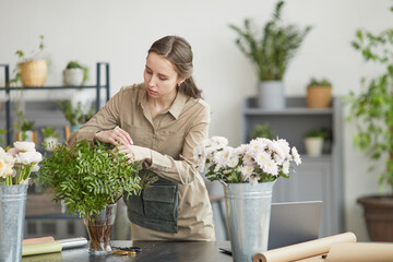 Portrait of young woman arranging flower compositions in green florists workshop, copy space