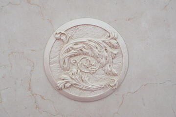 Close-up of a decorative element of the interior of a room - a round-shaped stucco molding (bas-relief) with an ornament on white marble