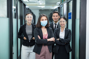 Fototapeta premium Confident asian business team wearing face mask, face shield standing crossed arms in the office