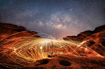 Man wielding spark fire swirl on rock reef canyon and holes with milky way in the night sky at Sam...
