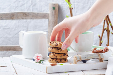 Female hands preparing breakfast with cookies on a white wooden tray for mom's day