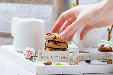 Female hands preparing breakfast with cookies on a white wooden tray for mom's day