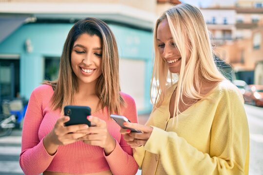 Two beautiful and young girl friends together having fun at the city using smartphone