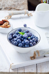 Fresh pickly blueberries for breakfast in ceramic bowl on a white wooden tray..
