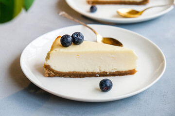 Slice of New York cheesecake on white plate. Sweet cake decorated fresh blueberries.