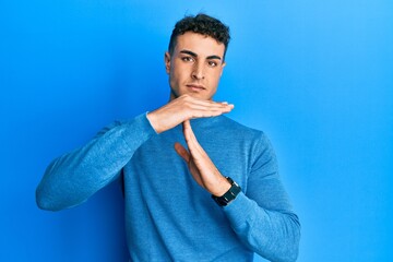 Hispanic young man wearing casual winter sweater doing time out gesture with hands, frustrated and...