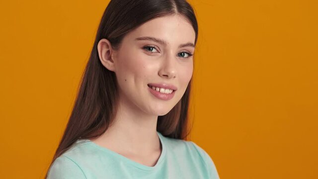 A beautiful young woman is winking while looking to the camera standing isolated over orange background in the studio