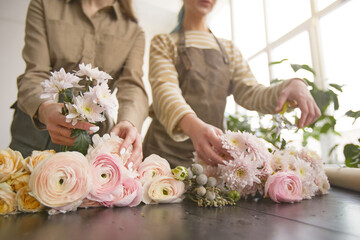 Close up of flowers on table in flower shop with two female florists arranging bouquets, copy space - obrazy, fototapety, plakaty
